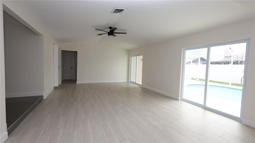 An empty room with light-colored tile flooring, a ceiling fan, and sliding glass doors — 9737 SAN VINCENTE WAY, PORT RICHEY, FL