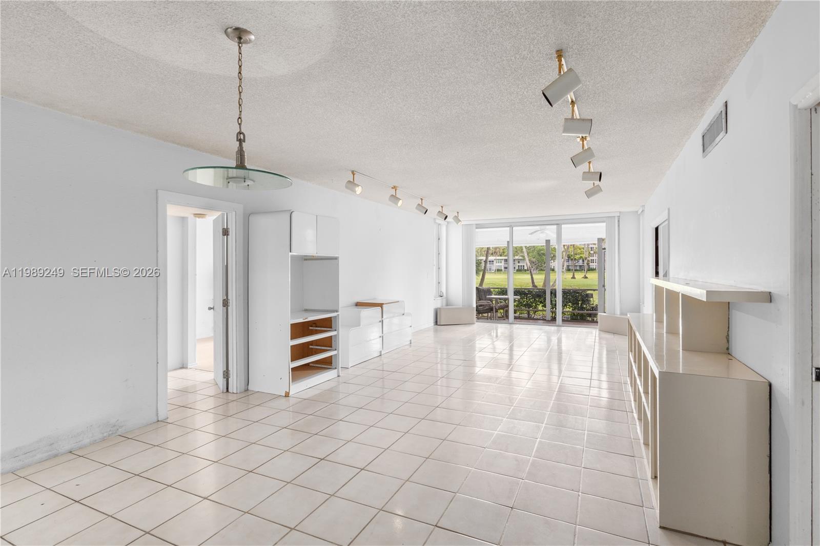 A bright, tiled living room features white built-in shelving, track lighting, and a sliding glass door — 806 Cypress Grove Ln # 111, Pompano Beach FL 33069, POMPANO BEACH, FL