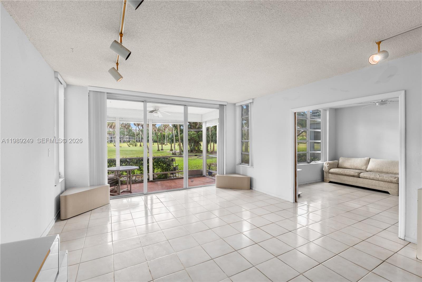 A bright living room features white tile floors, track lighting, and a view of a patio — 806 Cypress Grove Ln # 111, Pompano Beach FL 33069, POMPANO BEACH, FL