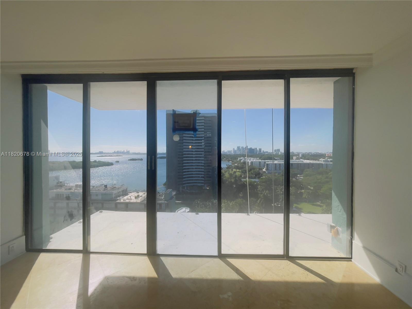 A room with floor-to-ceiling glass sliding doors overlooking a bay and city skyline — 780 NE 69th St # 1507, Miami FL 33138, MIAMI, FL