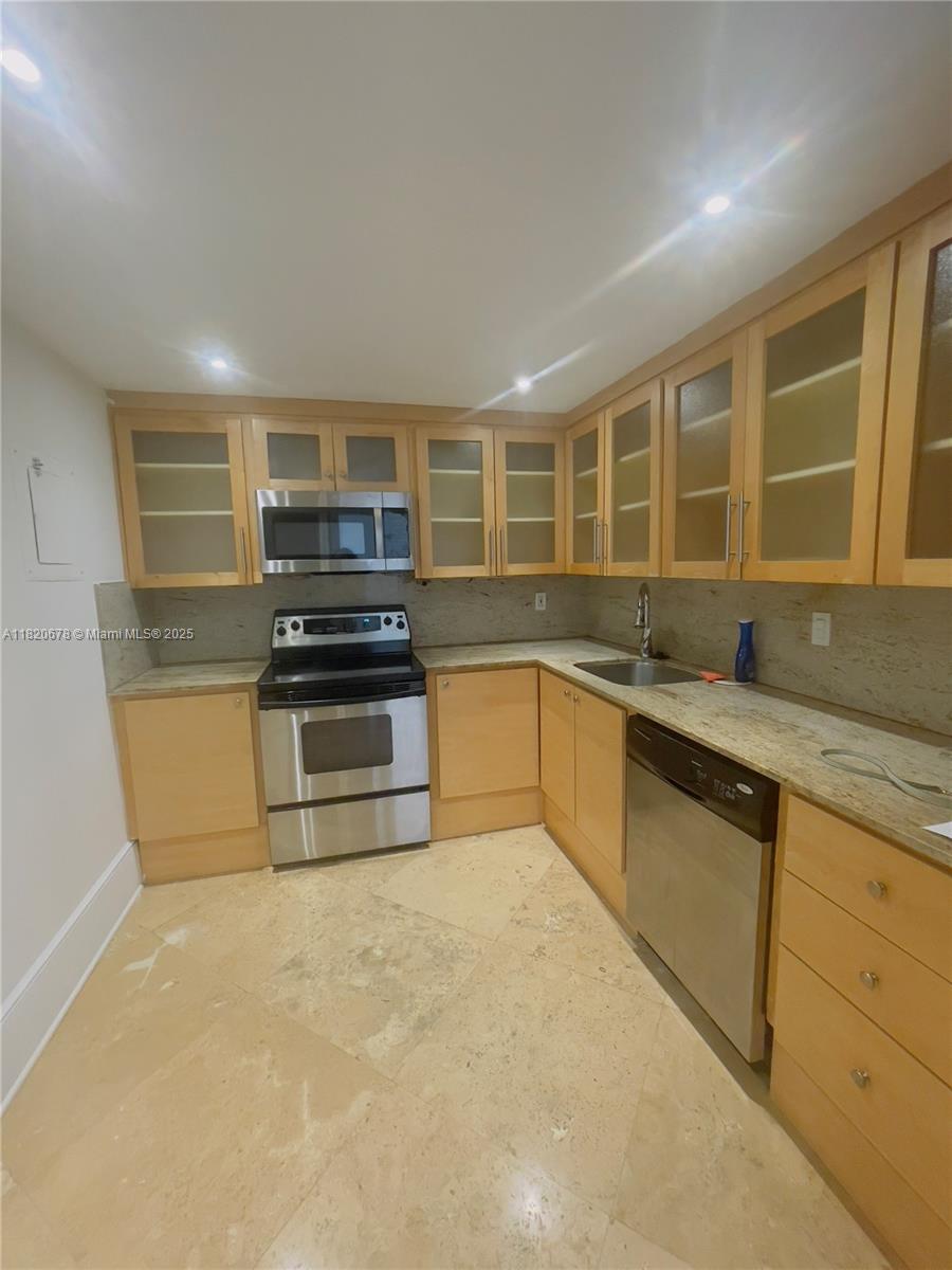 A kitchen features light wood cabinets, stainless steel appliances, and beige stone countertops and flooring — 780 NE 69th St # 1507, Miami FL 33138, MIAMI, FL