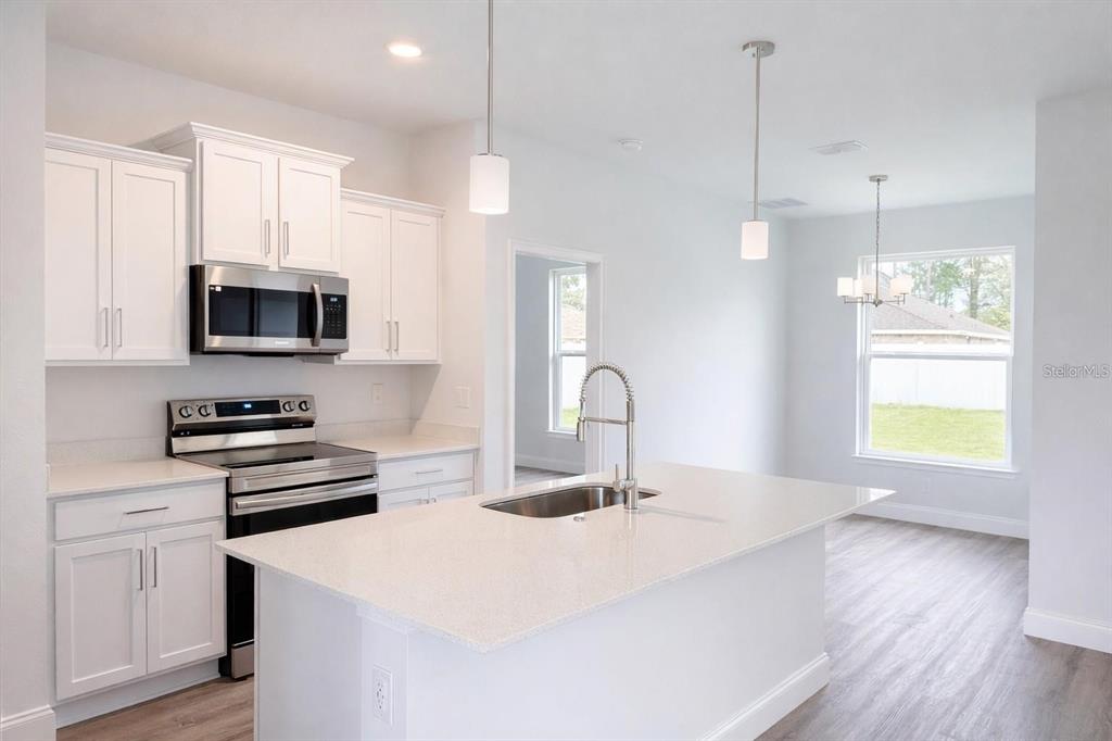 A modern kitchen features white cabinets, stainless steel appliances, a quartz island, and wood flooring — 15 BUD SHIRE LANE, PALM COAST, FL