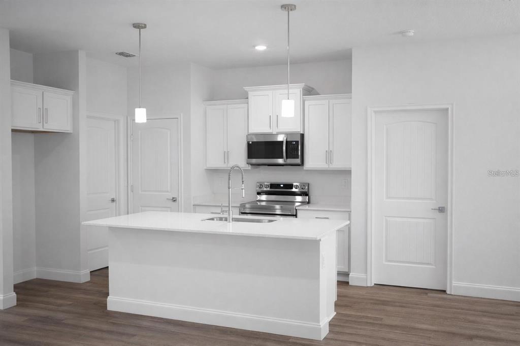 A modern kitchen features white cabinetry, stainless steel appliances, and a central island with seating — 15 BUD SHIRE LANE, PALM COAST, FL