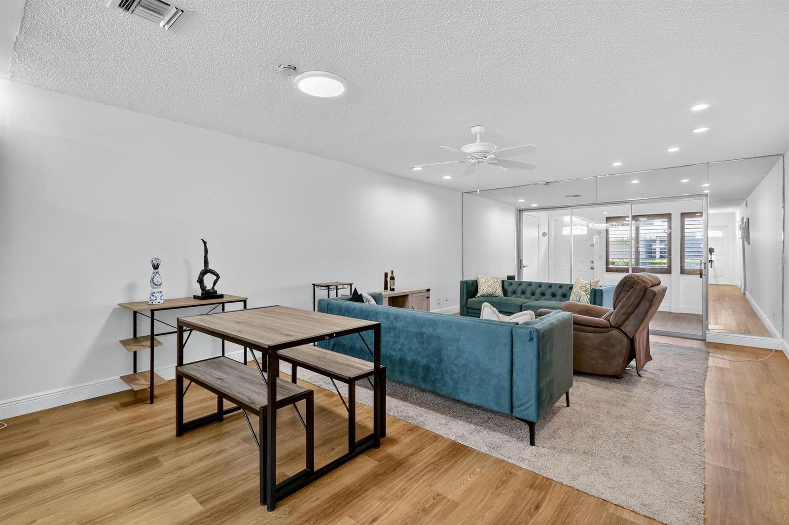 A living and dining area features wood-look flooring, a teal sofa, and a mirrored wall — 448 Franconia Circle # B, Lake Worth FL 33467, LAKE WORTH, FL