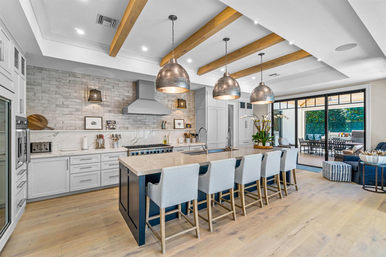 A kitchen features a large dark blue island, white cabinetry, brick backsplash, and wood ceiling beams — 18 NW 15th Street, Delray Beach FL 33444, DELRAY BEACH, FL