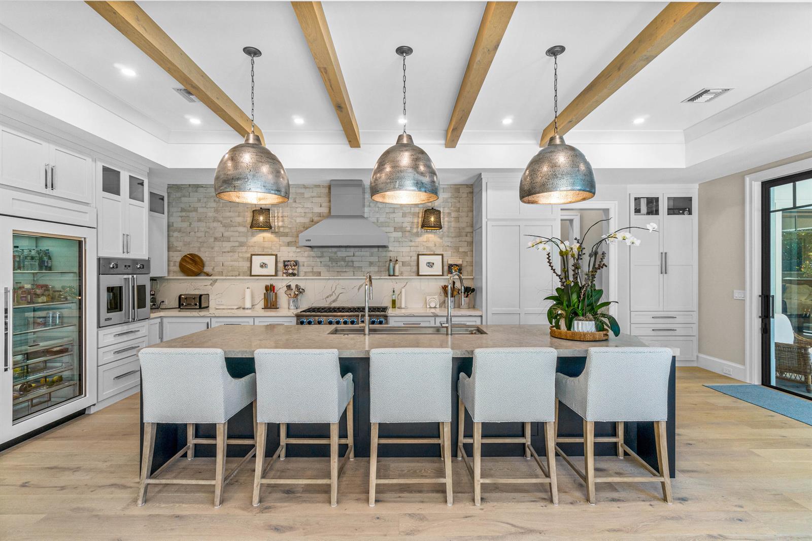 A kitchen features a large island with five chairs, pendant lighting, and wood ceiling beams — 18 NW 15th Street, Delray Beach FL 33444, DELRAY BEACH, FL