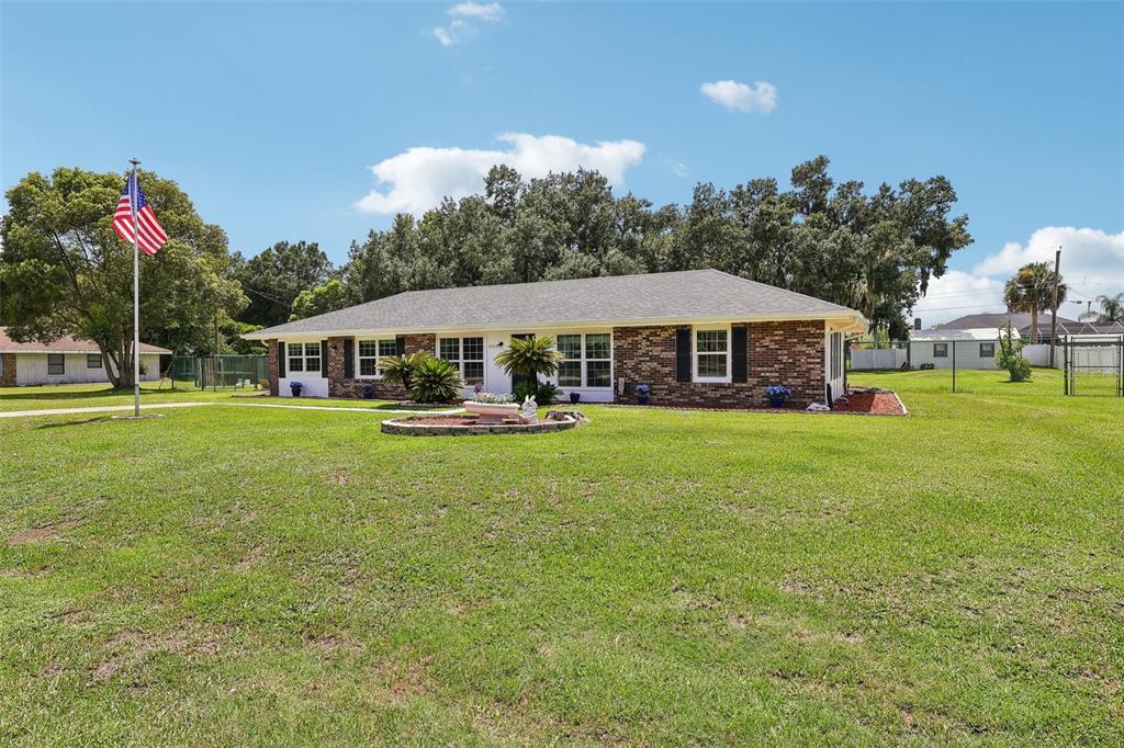 A single-story brick house with a large front lawn and an American flag — 6513 NEWMAN CIRCLE W, LAKELAND, FL