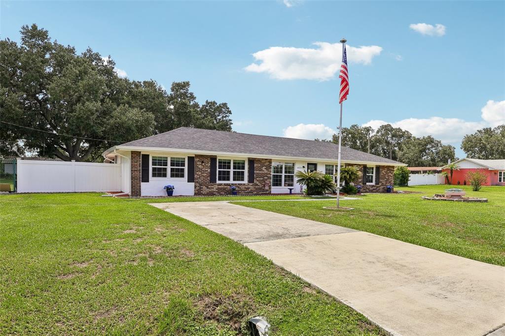 A single-story brick house with a concrete driveway and an American flag in the yard — 6513 NEWMAN CIRCLE W, LAKELAND, FL