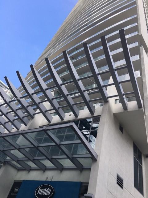 Low-angle view of a modern high-rise building with a prominent metal pergola and glass canopy — 1100 S Miami Ave # 1602, Miami FL 33130, MIAMI, FL