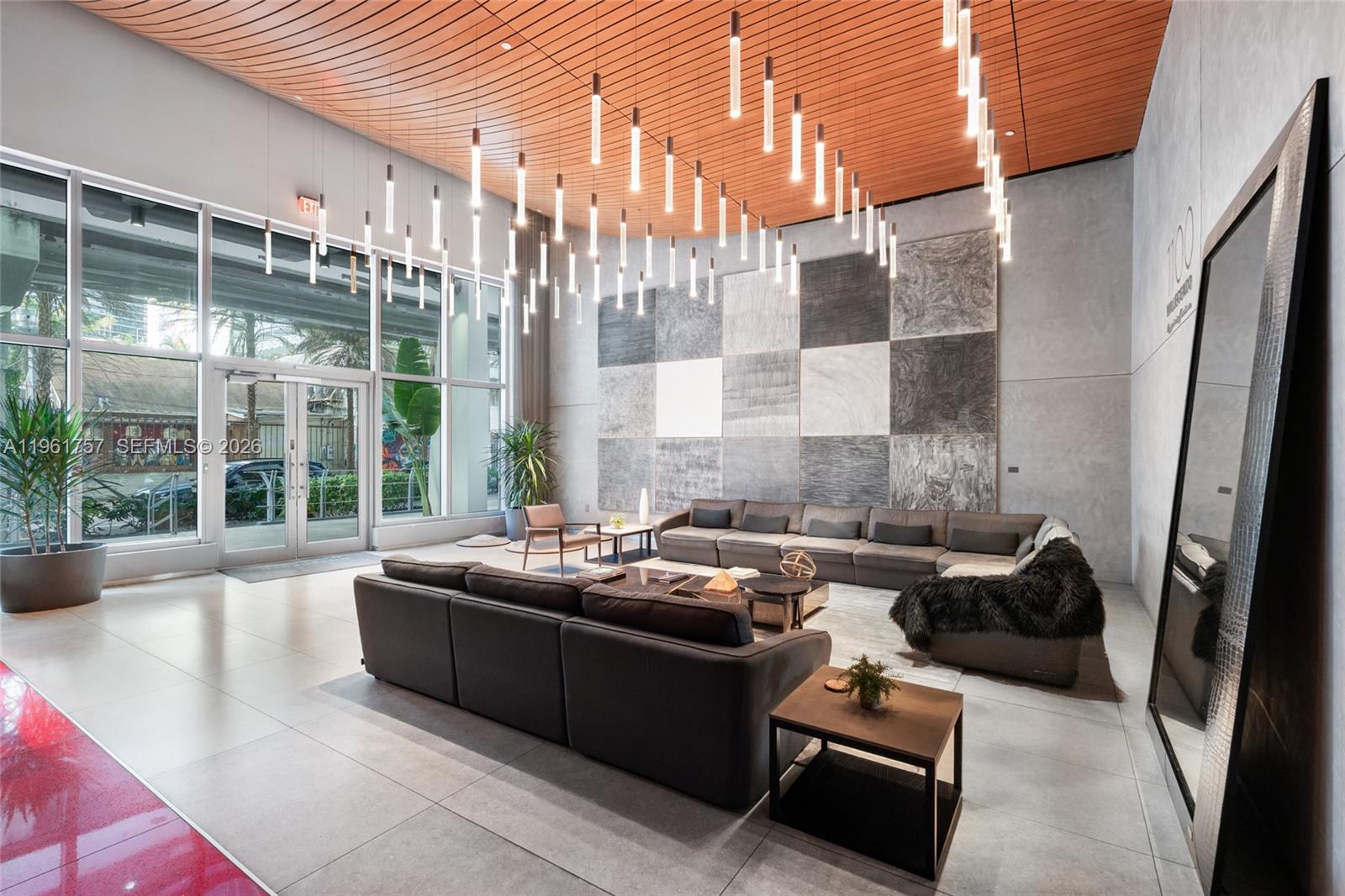 A modern lobby features a large sectional sofa, a checkered wall mural, and hanging lights — 1100 S Miami Ave # 1602, Miami FL 33130, MIAMI, FL