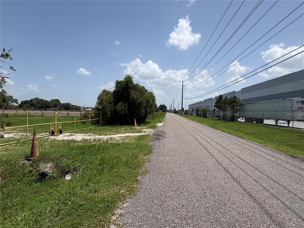 A paved road runs alongside a grassy area with a yellow fence and industrial buildings — 0 HAMILTON ROAD, LAKELAND, FL