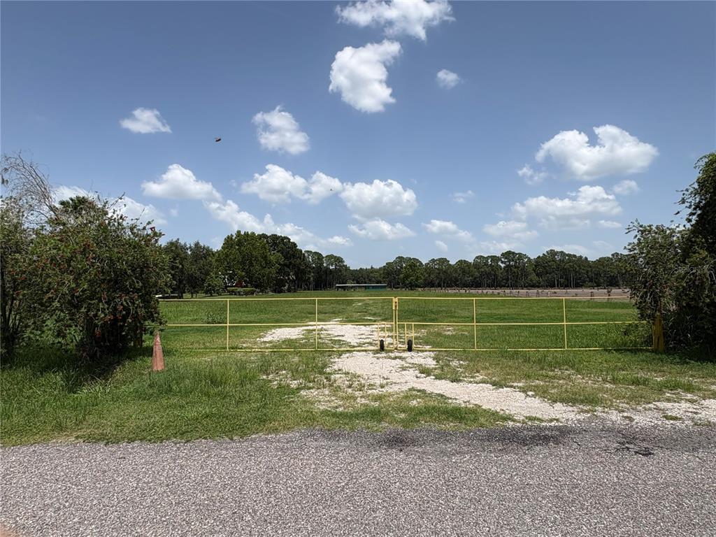 A yellow metal gate opens onto a grassy field with a gravel driveway — 0 HAMILTON ROAD, LAKELAND, FL