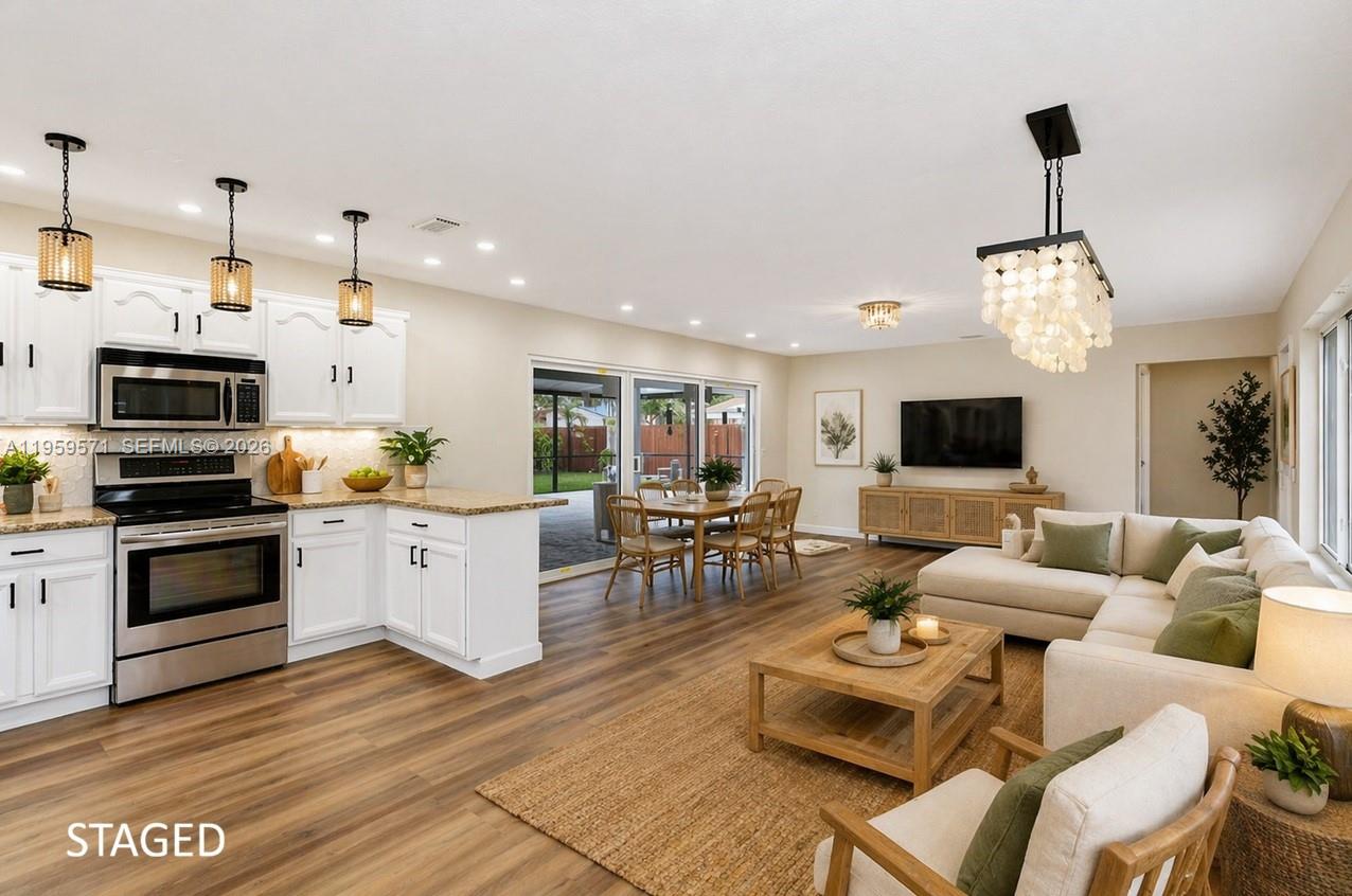 An open-concept kitchen, dining area, and living room with white cabinets and wood-look flooring — 1507 Harding St, Hollywood FL 33020, HOLLYWOOD, FL