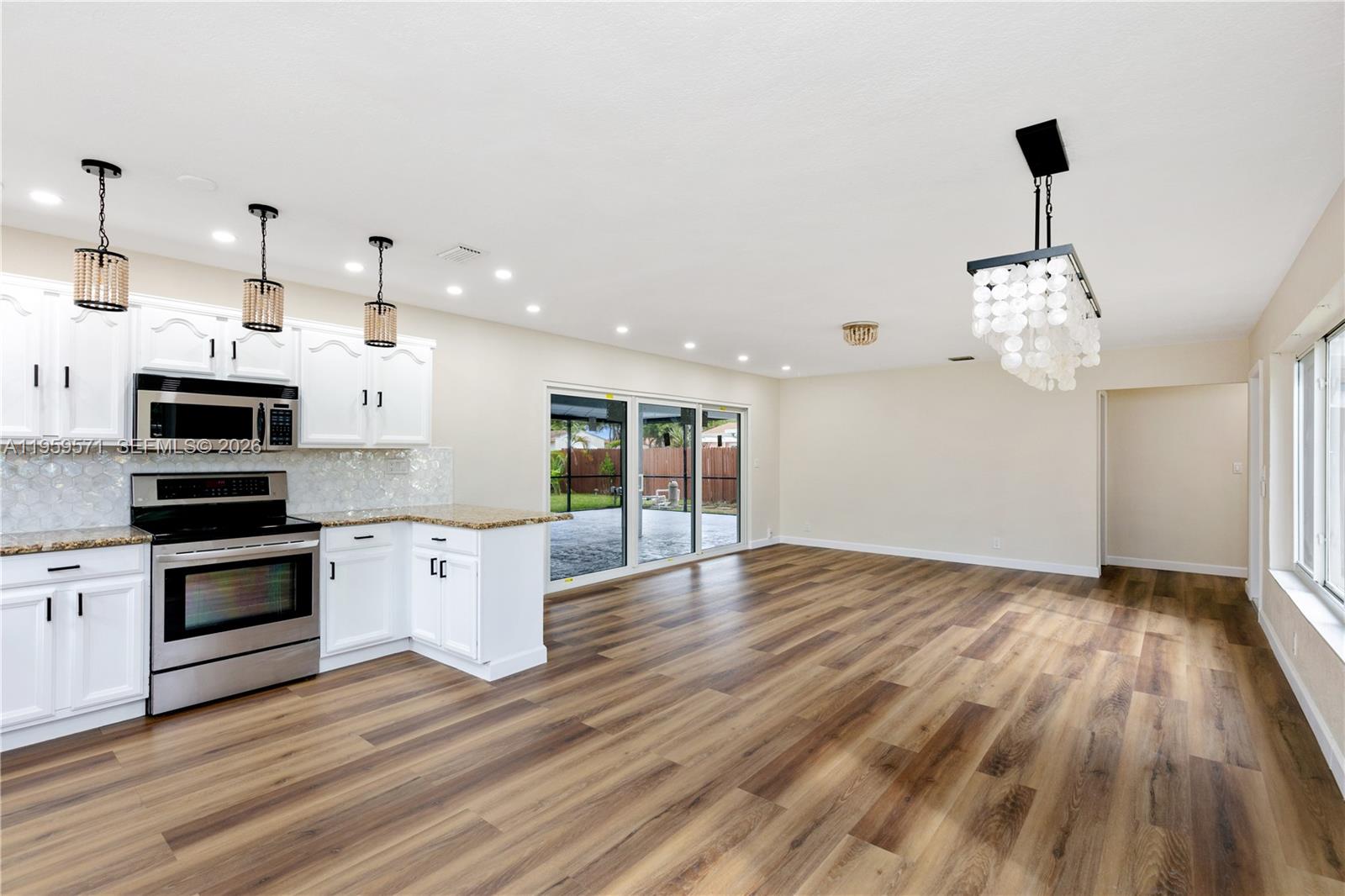 A kitchen with white cabinets and stainless steel appliances opens into a spacious living area — 1507 Harding St, Hollywood FL 33020, HOLLYWOOD, FL