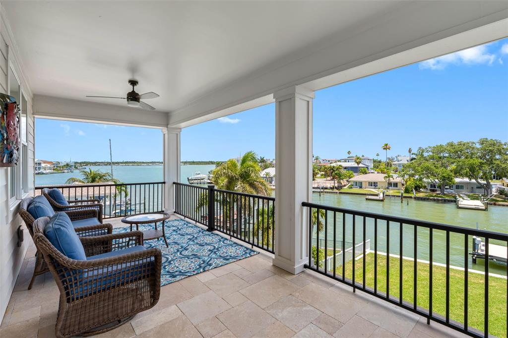 A covered balcony with wicker furniture overlooks a canal and residential waterfront properties — 16025 REDINGTON DRIVE, REDINGTON BEACH, FL