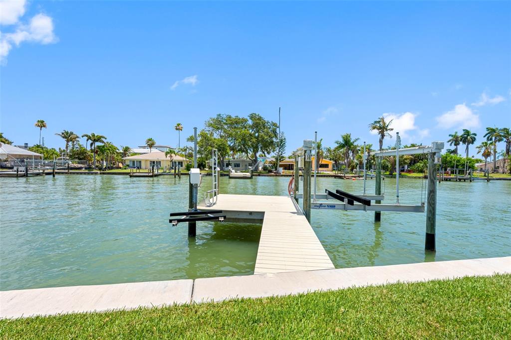 A wooden boat dock with a lift extends into a canal lined with palm trees — 16025 REDINGTON DRIVE, REDINGTON BEACH, FL