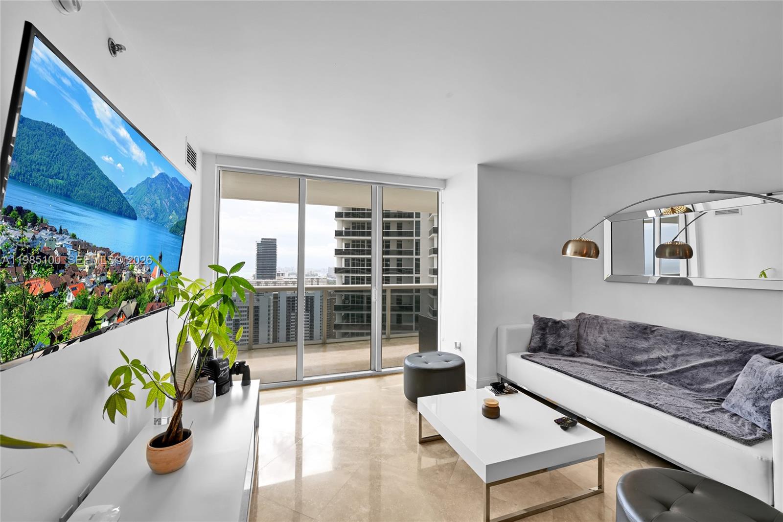 A modern living room features a white sofa, coffee table, television, and a balcony view — 1830 S Ocean Dr # 3104, Hallandale Beach FL 33009, HALLANDALE BEACH, FL