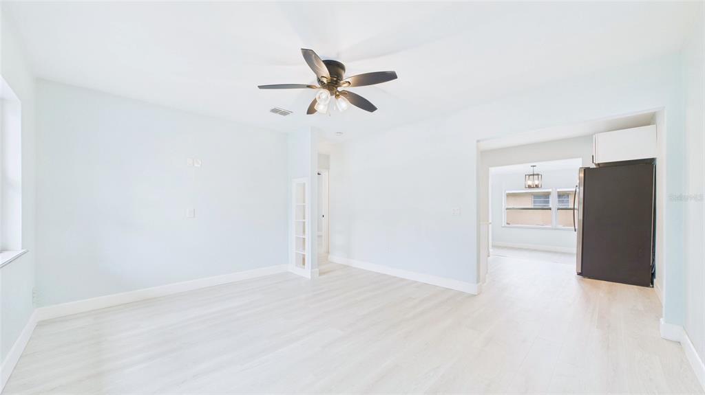 An empty room with light-colored wood flooring, a ceiling fan, and a view into a kitchen — 5312 BERKLEY ROAD, NEW PORT RICHEY, FL