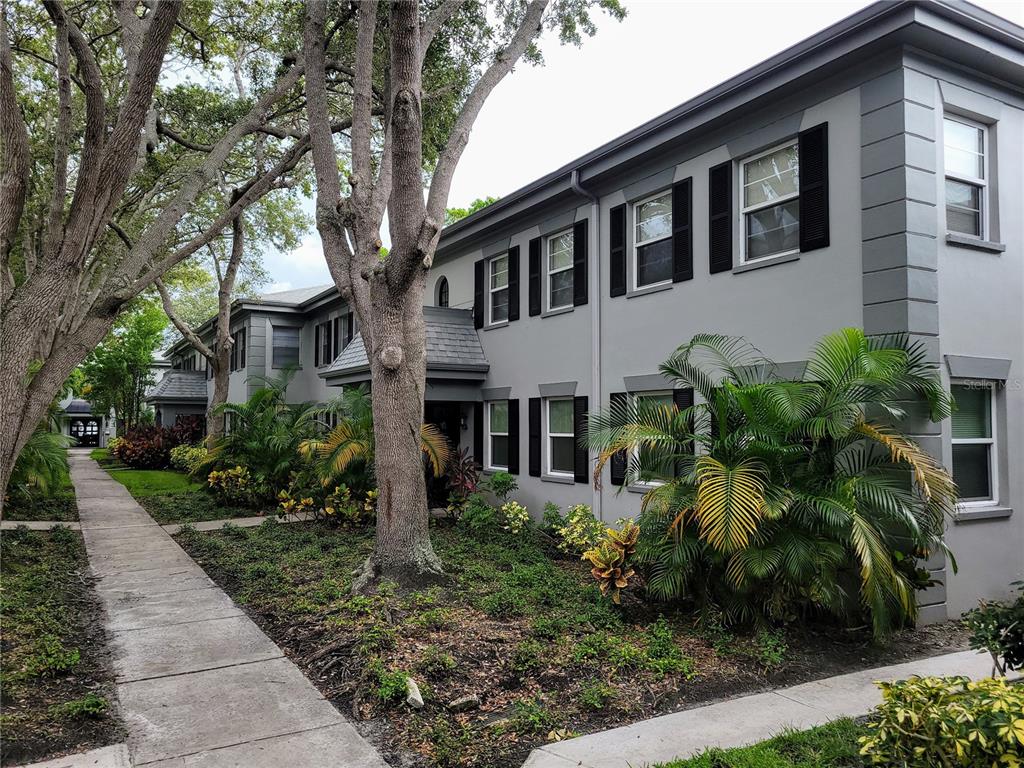 A two-story gray apartment building with black shutters sits behind a sidewalk and palm trees — 6925-A AVENUE DES PALAIS UNIT 1A, SOUTH PASADENA, FL