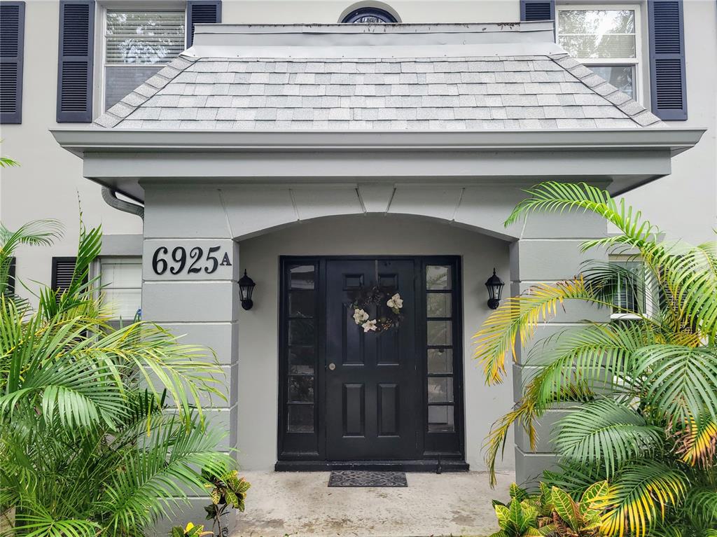 The exterior of a home features a gray front door, a shingled entryway, and palm plants — 6925-A AVENUE DES PALAIS UNIT 1A, SOUTH PASADENA, FL
