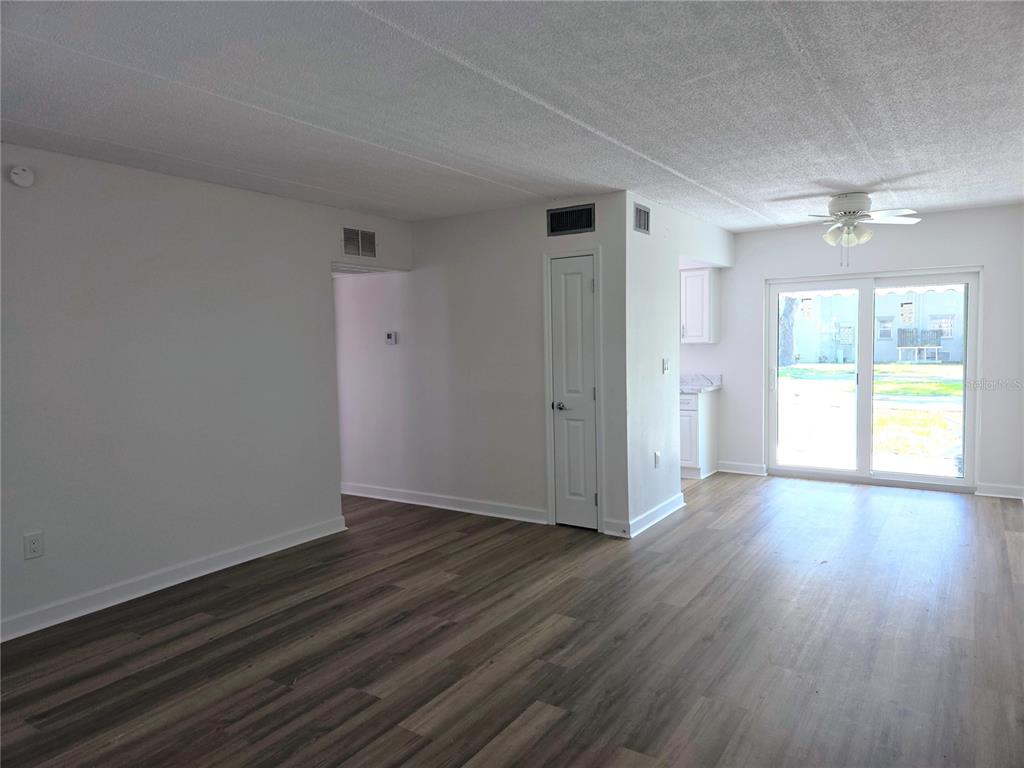 An empty living room features wood-look flooring, a ceiling fan, and sliding glass patio doors — 6925-A AVENUE DES PALAIS UNIT 1A, SOUTH PASADENA, FL