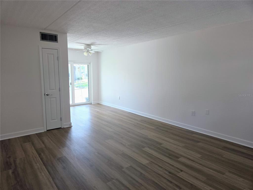 An empty room with light wood-look flooring, white walls, a ceiling fan, and sliding glass doors — 6925-A AVENUE DES PALAIS UNIT 1A, SOUTH PASADENA, FL