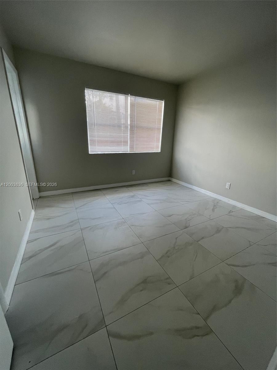An empty room features light-colored walls, a window with blinds, and large white marble-patterned floor tiles — 1101 S K St # 16, Lake Worth FL 33460, LAKE WORTH, FL