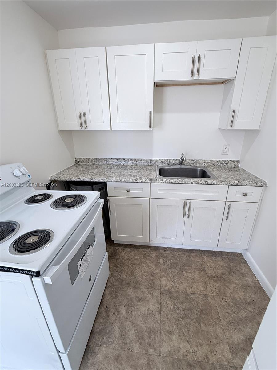 A small kitchen features white cabinets, a granite countertop, a sink, and an electric stove — 1101 S K St # 16, Lake Worth FL 33460, LAKE WORTH, FL