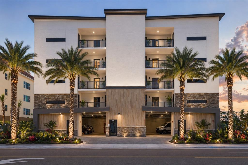 A four-story apartment building with a stone facade, balconies, and ground-level parking at dusk — 14048 GULF BOULEVARD UNIT 302, MADEIRA BEACH, FL