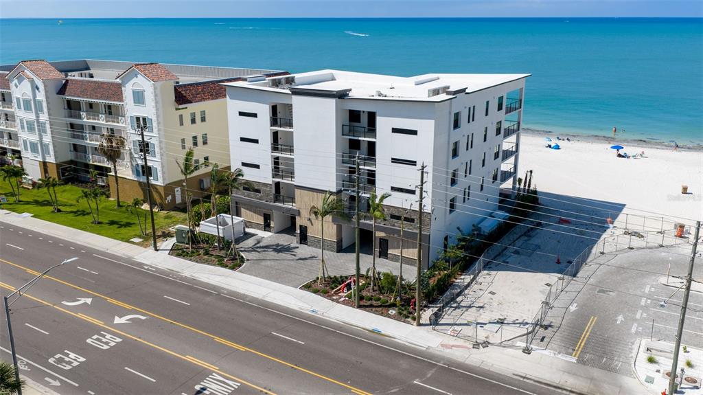An aerial view shows a modern white building situated next to a beach — 14048 GULF BOULEVARD UNIT 302, MADEIRA BEACH, FL