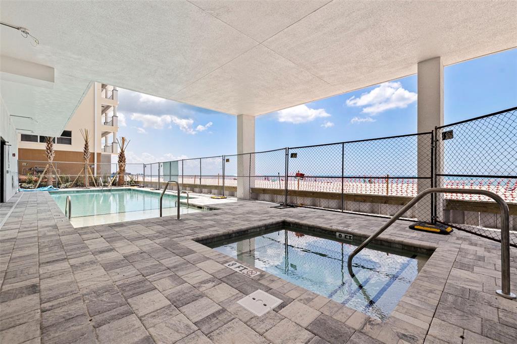 An outdoor pool and hot tub area with pavers, a chain-link fence, and beach views — 14048 GULF BOULEVARD UNIT 302, MADEIRA BEACH, FL