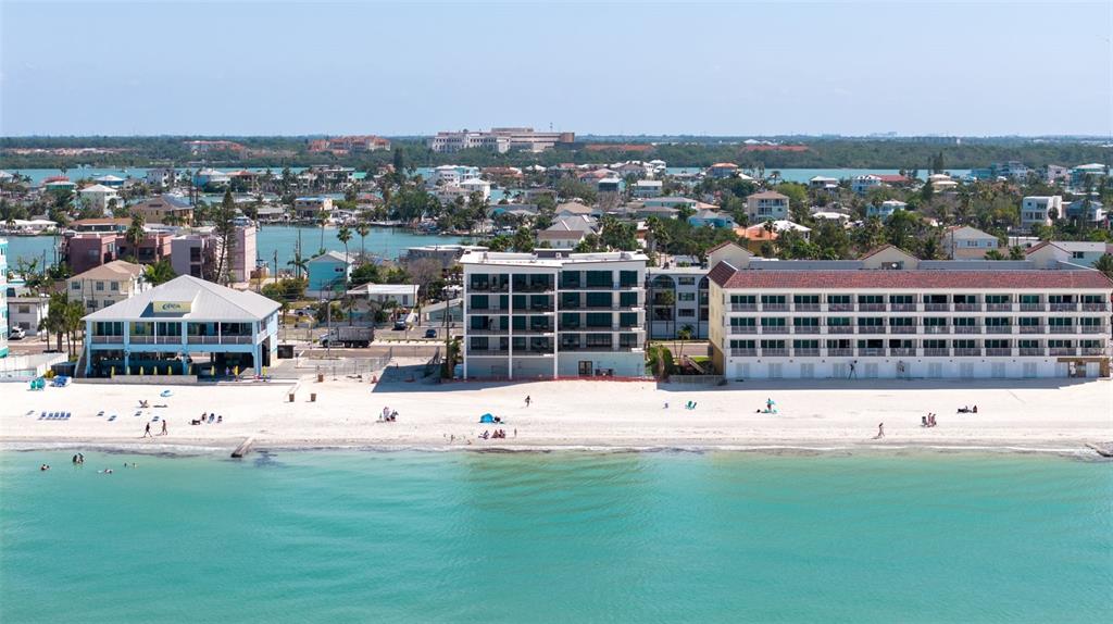 An aerial view shows beachfront buildings, a sandy beach, and turquoise water under a clear sky — 14048 GULF BOULEVARD UNIT 302, MADEIRA BEACH, FL
