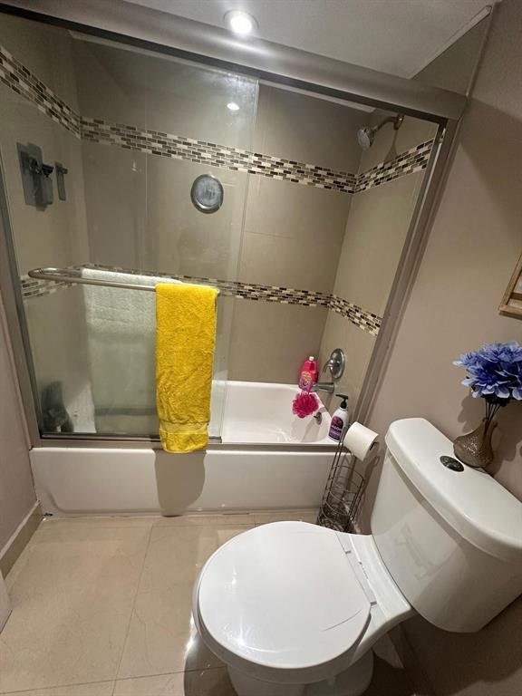 A bathroom features a tiled shower-tub combination with glass doors and a white toilet — 661 NE 195TH STREET UNIT 402, MIAMI, FL