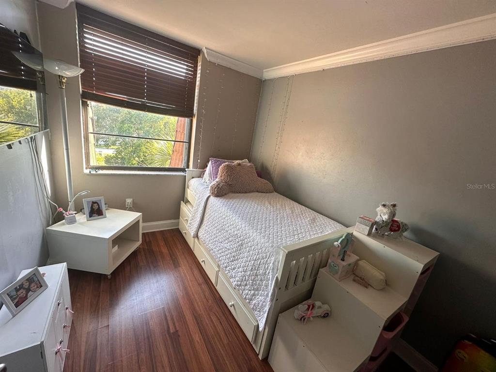 A bedroom features a twin bed with storage drawers, wood-look flooring, and a large window — 661 NE 195TH STREET UNIT 402, MIAMI, FL