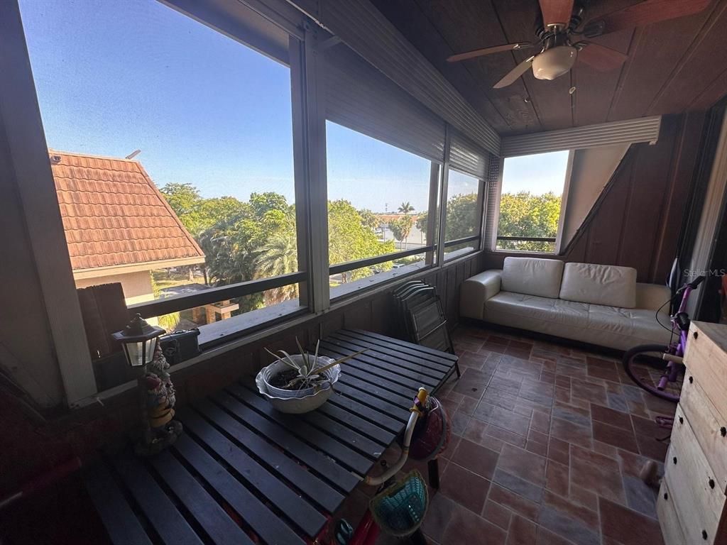 A screened-in porch features a wooden table, a white sofa, and tile flooring — 661 NE 195TH STREET UNIT 402, MIAMI, FL
