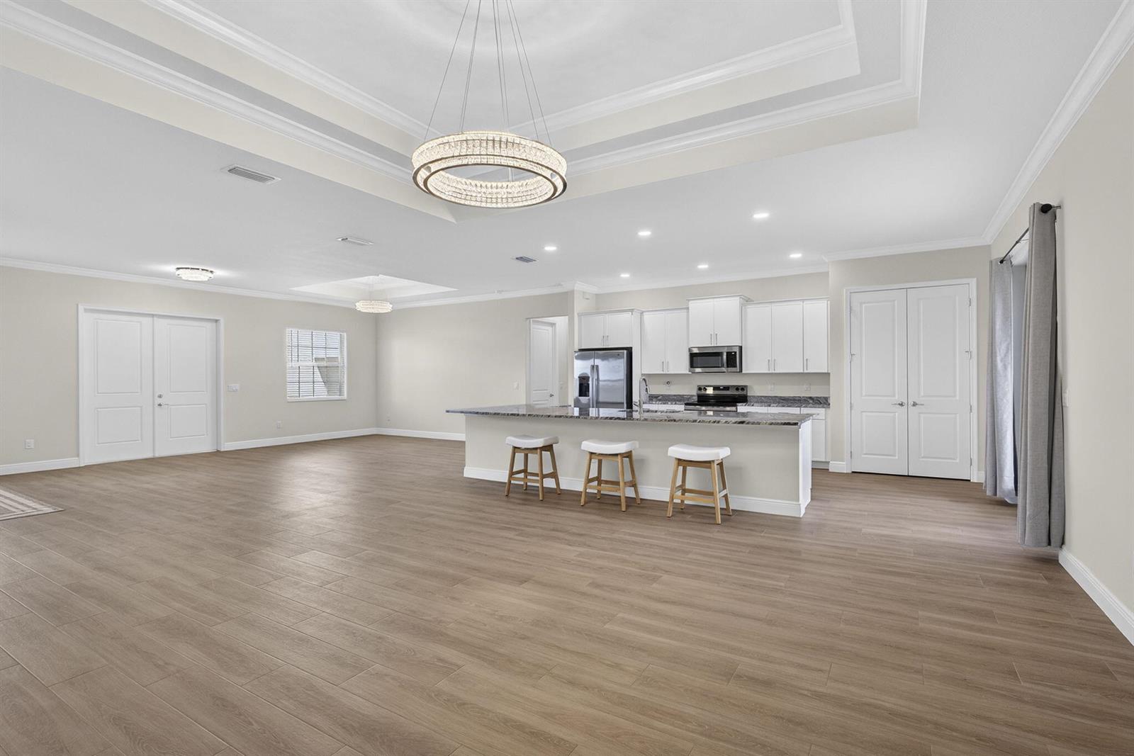 A spacious open-concept kitchen and living area featuring light wood flooring and white cabinetry — 14043 87th Street N, Loxahatchee FL 33470, LOXAHATCHEE, FL