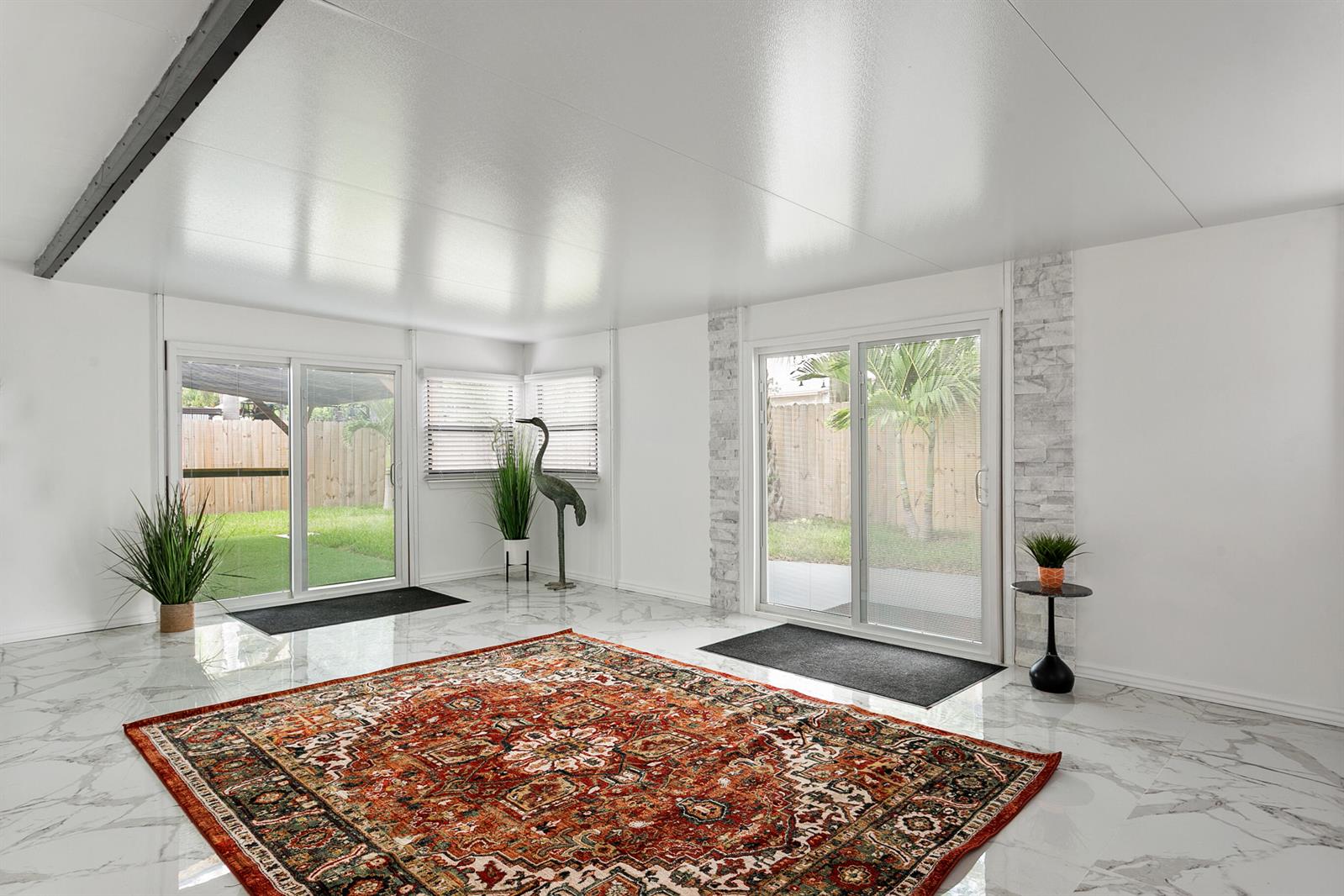 A bright sunroom features white marble-look tile flooring, a large patterned rug, and sliding glass doors — 3141 NE 14th Avenue, Pompano Beach FL 33064, POMPANO BEACH, FL