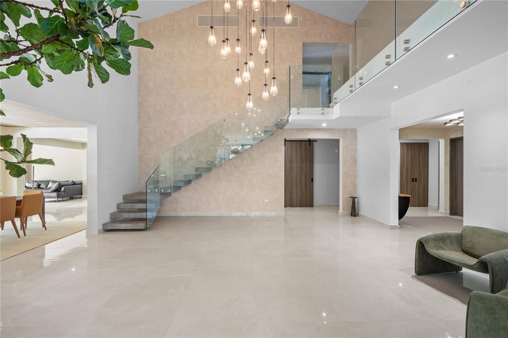 A spacious, modern foyer features a floating staircase, glass railings, and a multi-pendant light fixture — 366 DORADO BEACH EAST, DORADO, PR