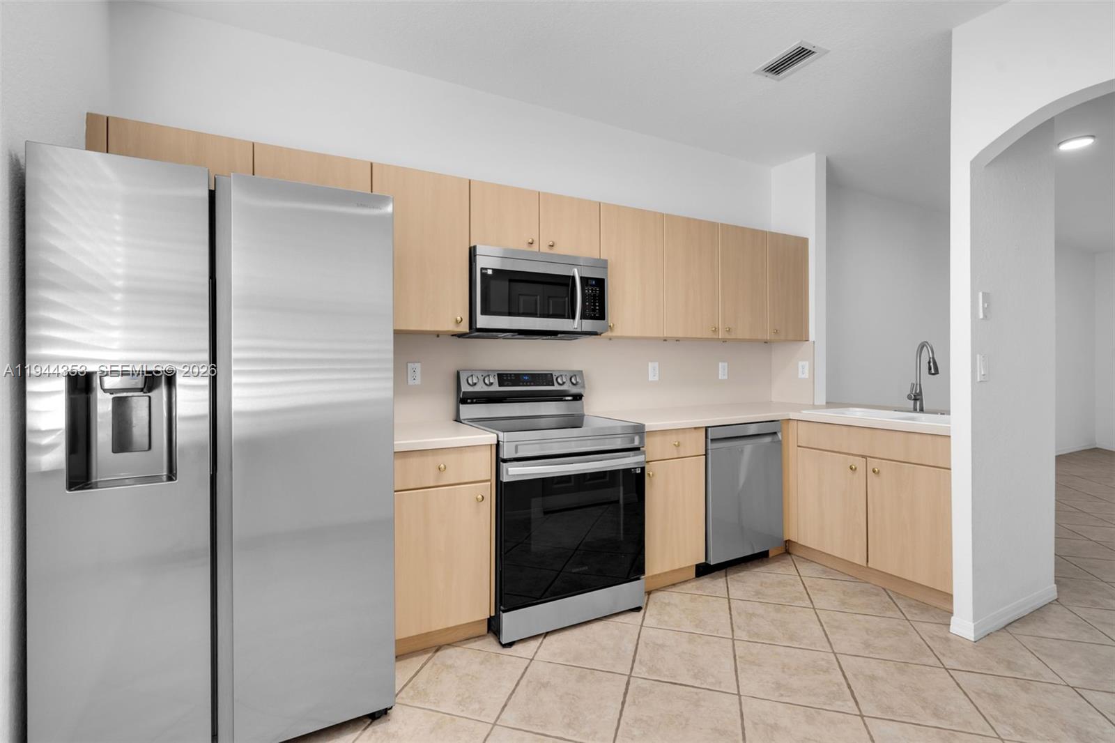 A kitchen features light wood cabinets, stainless steel appliances, and beige tile flooring — 5670 NW 116th Ave # 219, Doral FL 33178, DORAL, FL