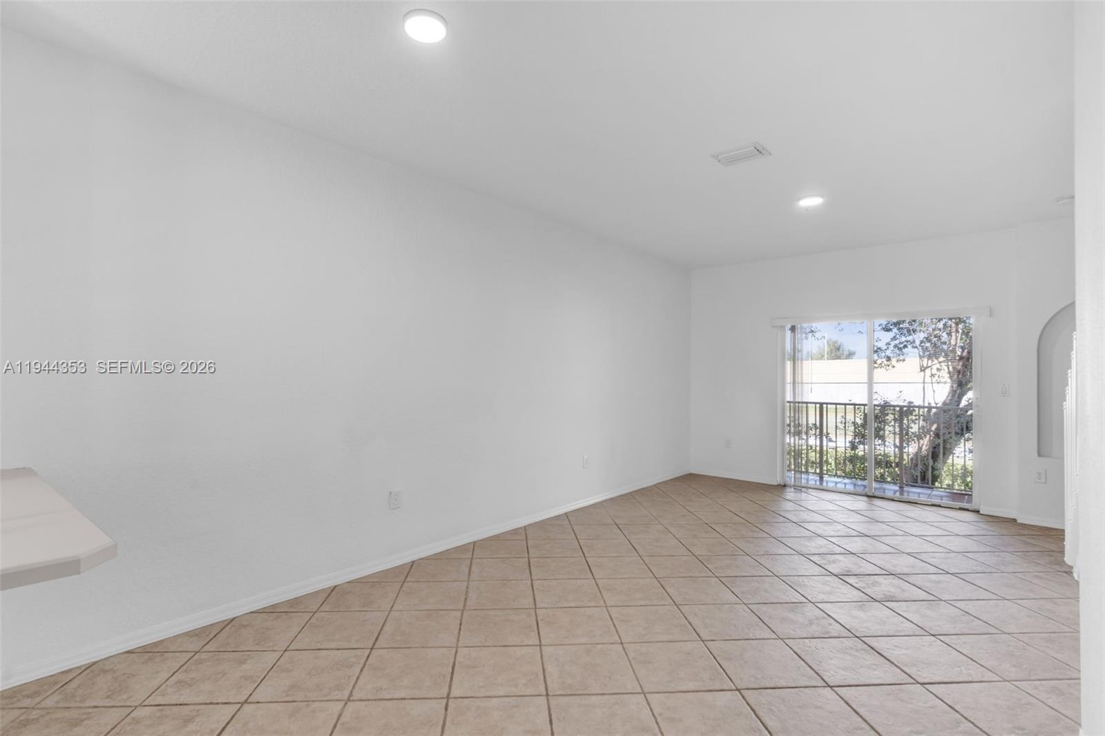 An empty room features white walls, beige tile flooring, recessed lighting, and a sliding glass door — 5670 NW 116th Ave # 219, Doral FL 33178, DORAL, FL