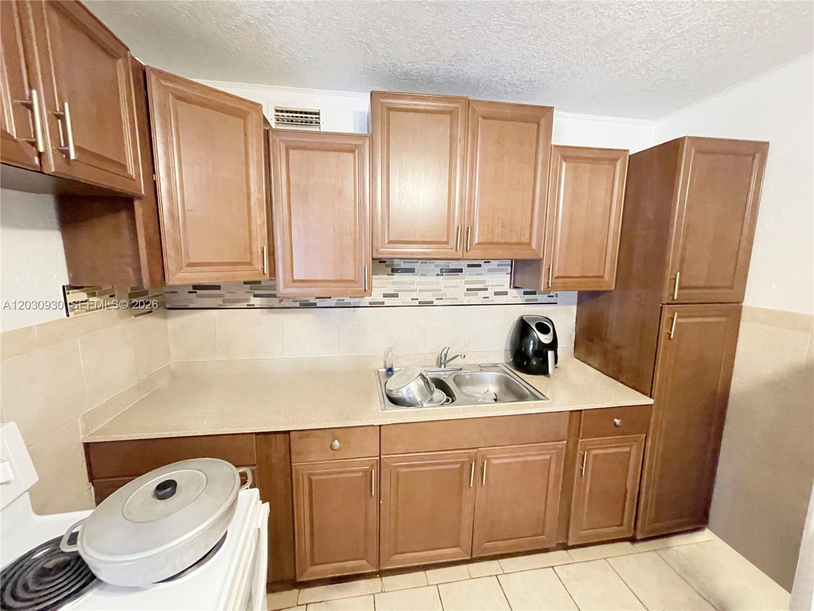 A kitchen features wood cabinets, a beige countertop, a double sink, and tiled backsplash — 1829 N A St # 51, Lake Worth FL 33460, LAKE WORTH, FL