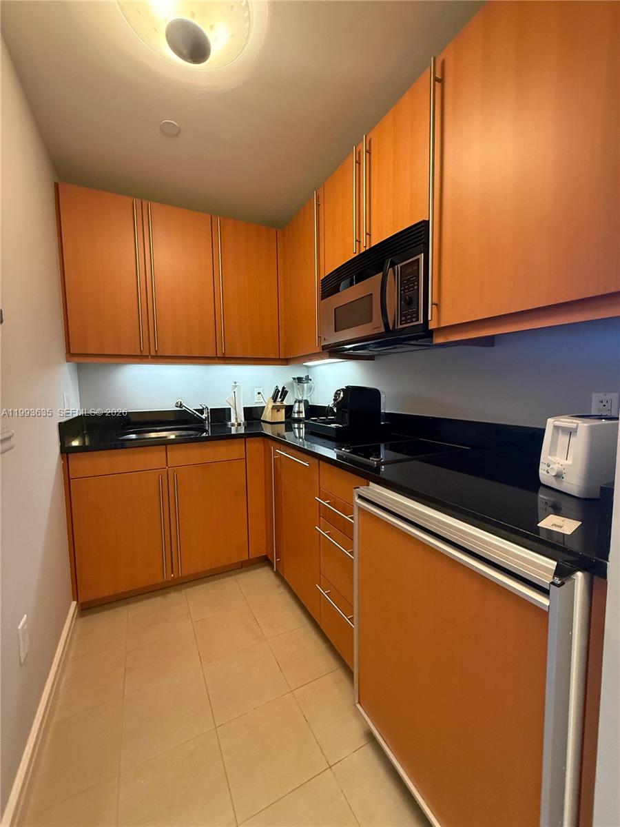A galley-style kitchen features wood cabinets, black countertops, and stainless steel appliances — 1435 Brickell Ave # 3305, Miami FL 33131, MIAMI, FL