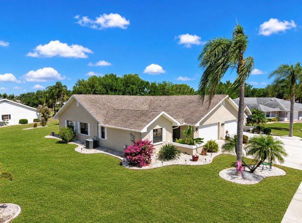 An exterior view of a single-story beige house with a tan roof and palm trees — 319 LINGER LANE, SUN CITY CENTER, FL