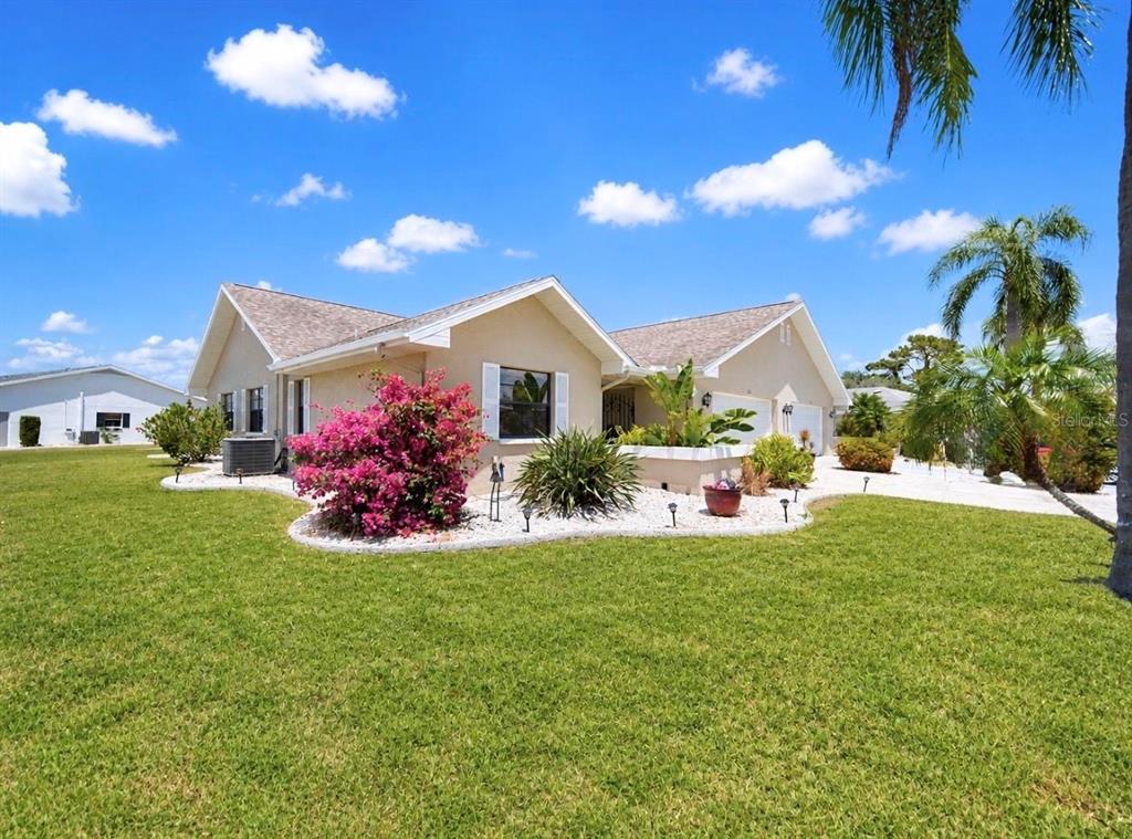 A single-story house with a beige stucco exterior, a landscaped front yard, and palm trees — 319 LINGER LANE, SUN CITY CENTER, FL