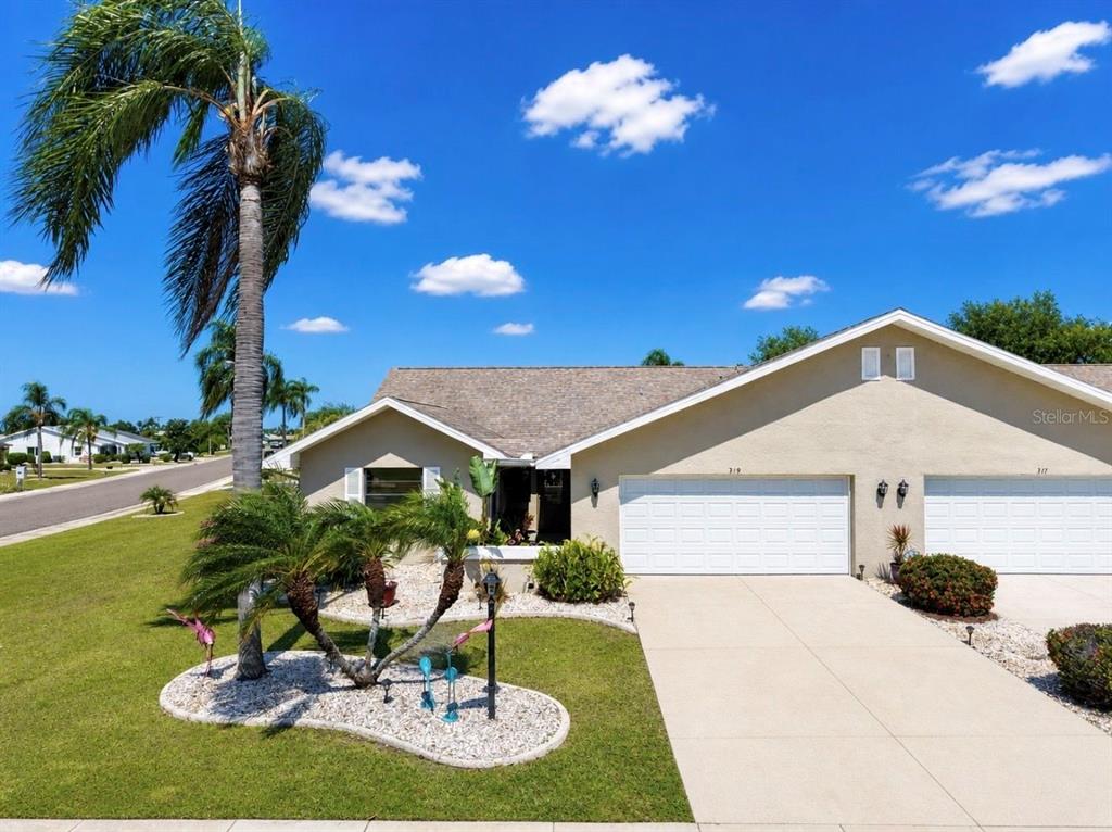 A single-story house with a two-car garage, beige stucco exterior, and palm trees in front — 319 LINGER LANE, SUN CITY CENTER, FL