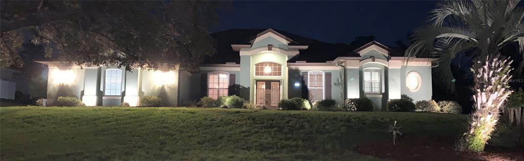 A teal single-story house with a prominent central entryway and exterior landscape lighting at night — 1 MINTWOOD POINT, HOMOSASSA, FL