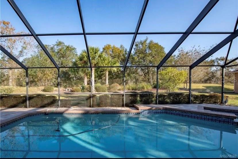 A swimming pool sits inside a screened-in lanai overlooking a grassy yard and trees — 1 MINTWOOD POINT, HOMOSASSA, FL