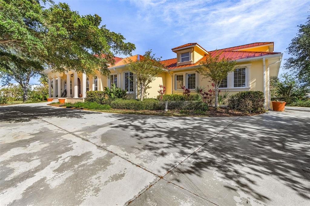 A yellow house with a red metal roof and a large concrete driveway — 21370 HARBORSIDE BOULEVARD, PORT CHARLOTTE, FL