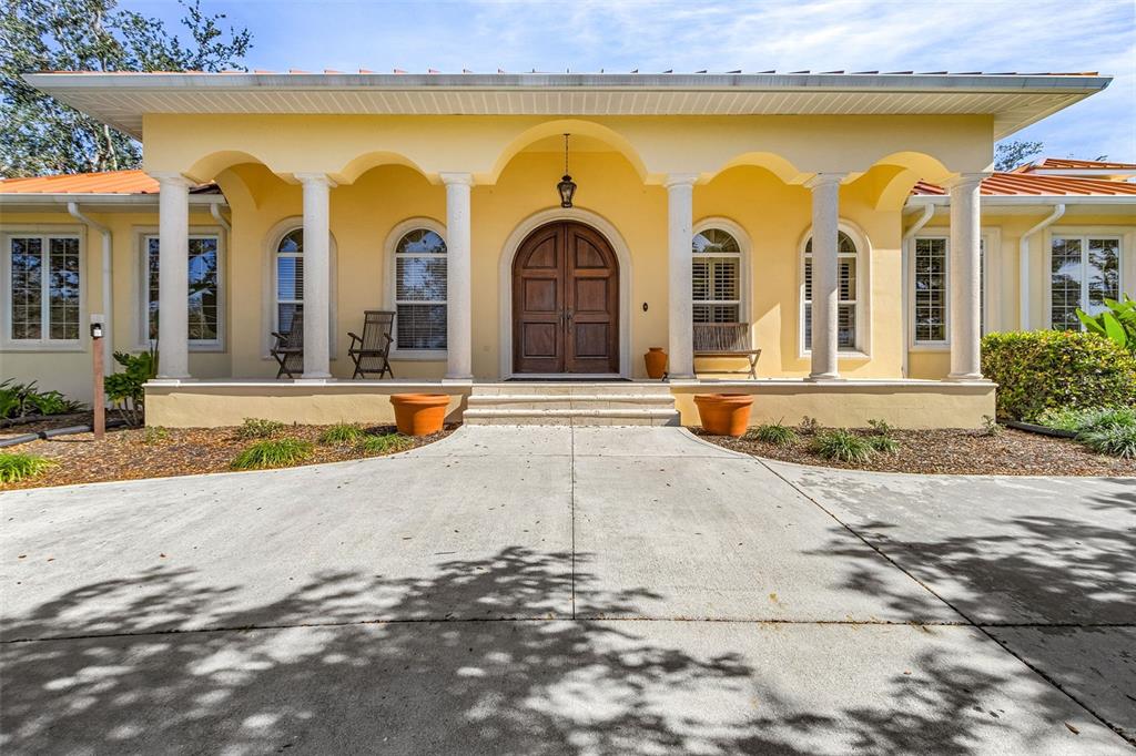 A yellow house exterior features a covered porch with white columns and a wooden door — 21370 HARBORSIDE BOULEVARD, PORT CHARLOTTE, FL