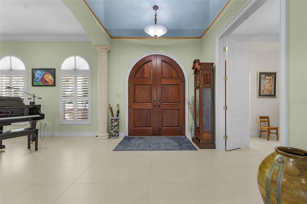 An entryway features a large arched wooden door, a grand piano, and light-colored tile flooring — 21370 HARBORSIDE BOULEVARD, PORT CHARLOTTE, FL